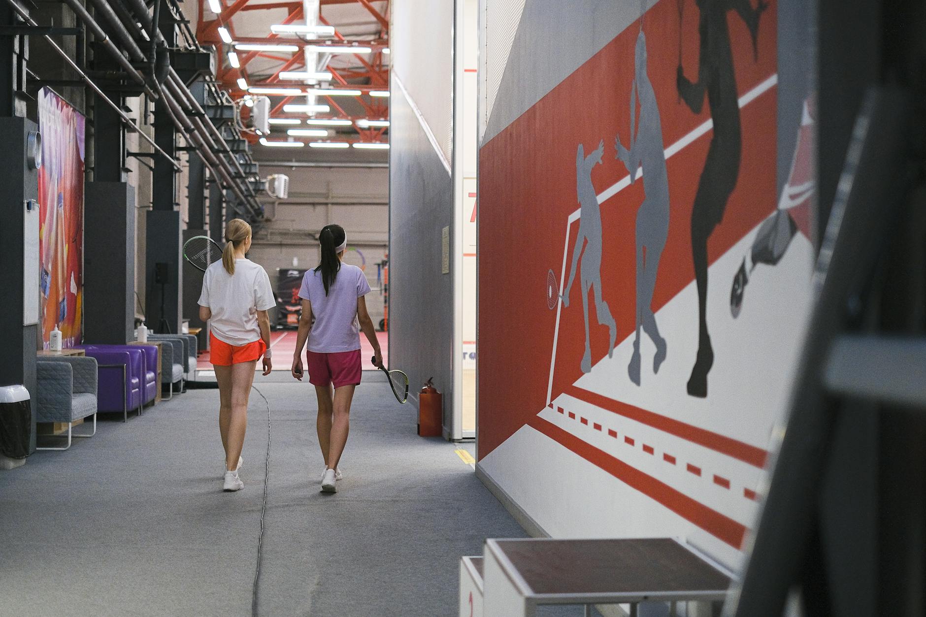 Dwie nastolatki z rakietami spacerują po hali sportowej