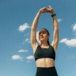 Kobieta w sportowym staniku rozciąga się na tle błękitnego nieba