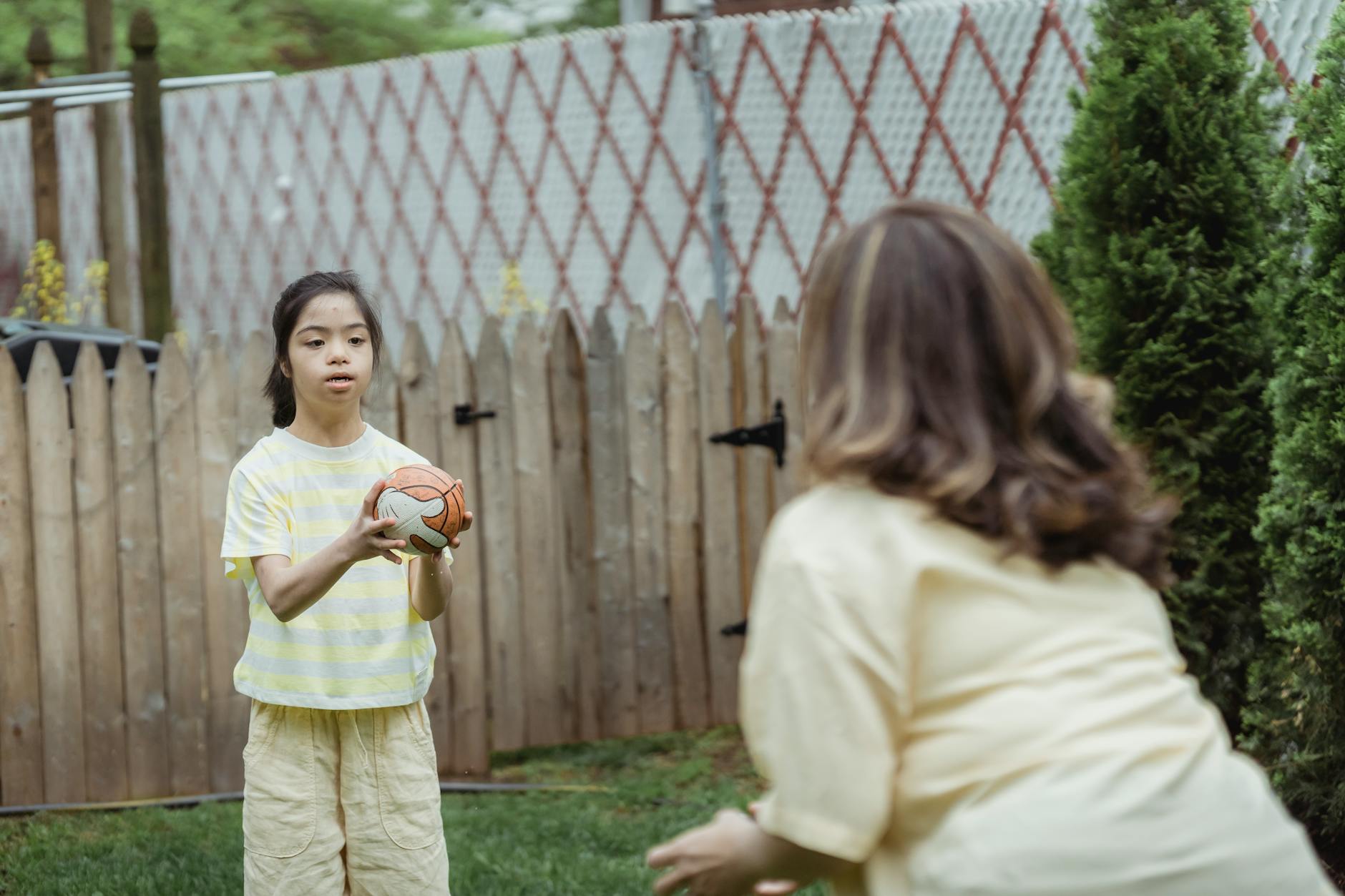 Mama bawi się z córką w rzucanie małą piłką do kosza na dworze