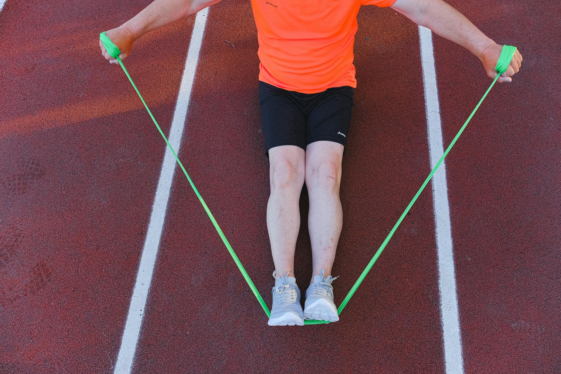 Mężczyzna ćwiczy z zieloną gumą oporową na bieżni stadionu