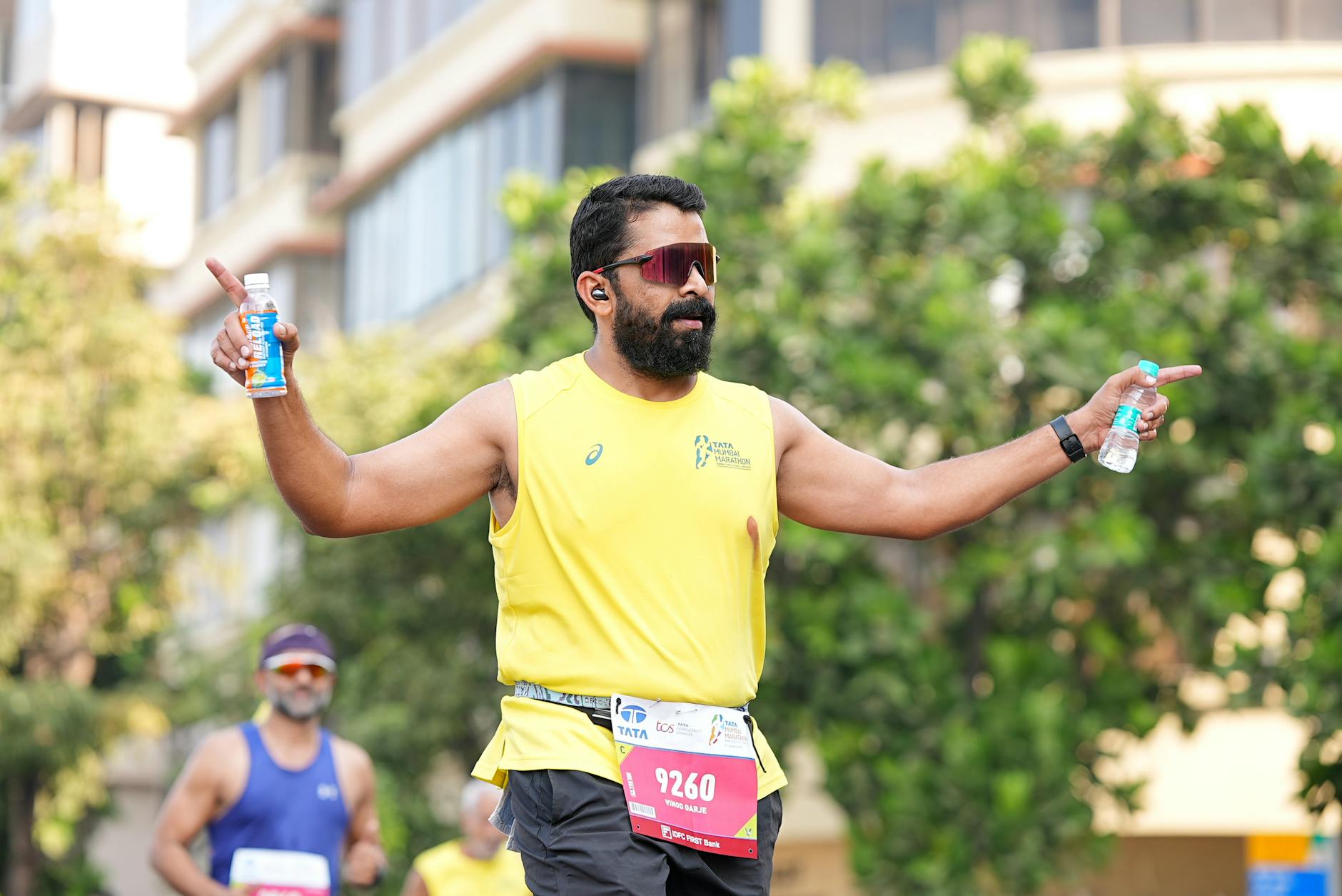 Biegacz w żółtej koszulce na maratonie trzymający napoje