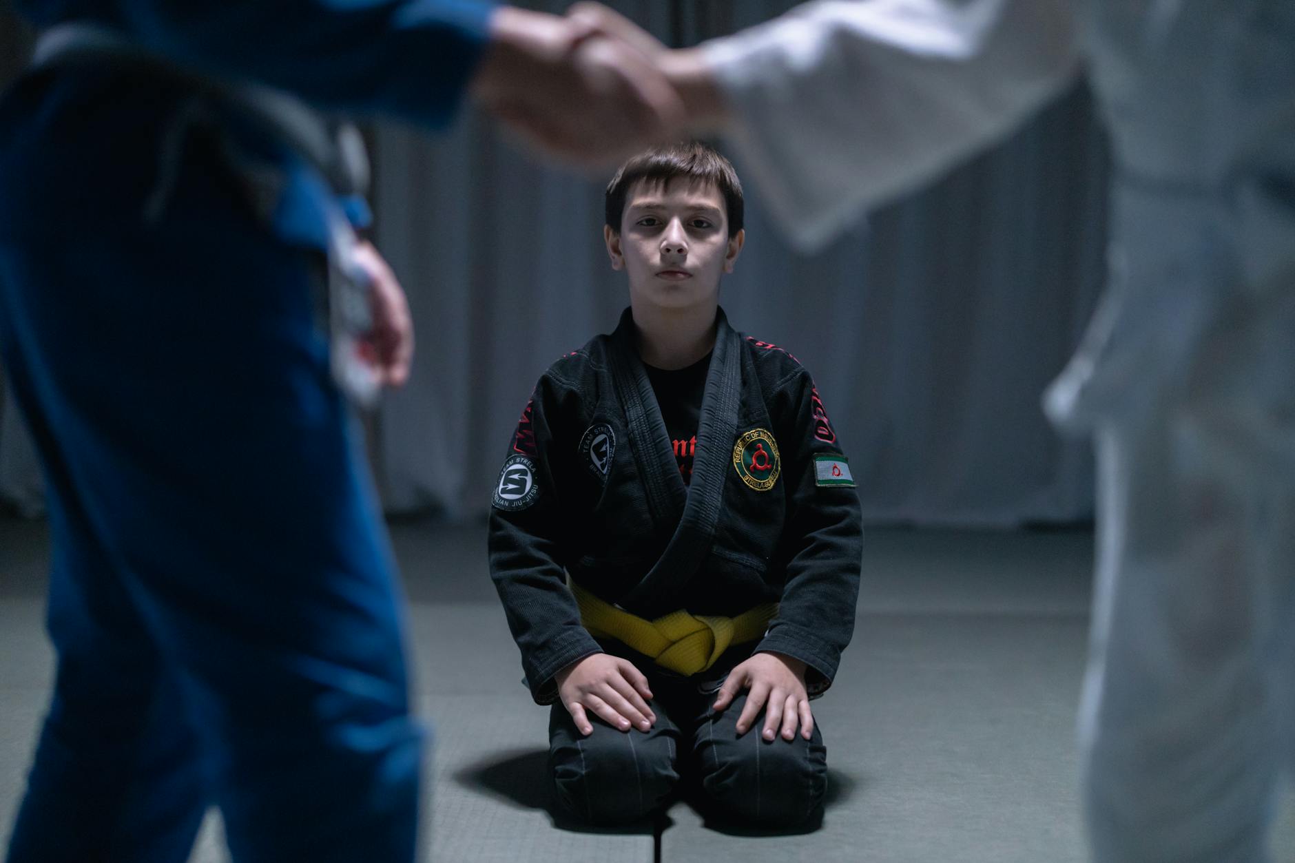 Chłopiec w żółtym pasie klęczy na macie podczas treningu jiu jitsu