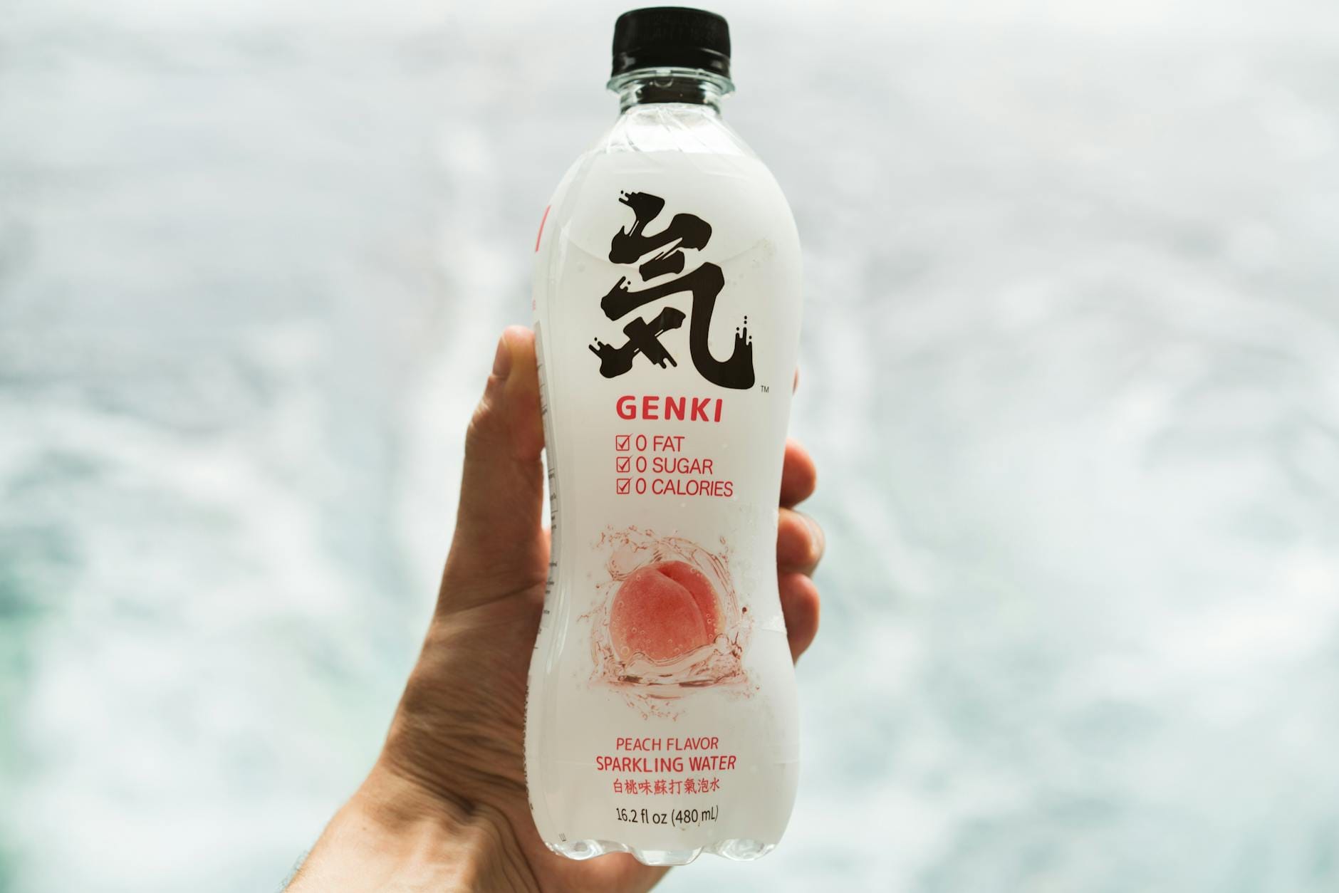 Dłoń trzymająca butelkę napoju gazowanego Genki o smaku brzoskwini