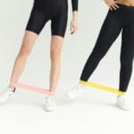 Dwie kobiety ćwiczą nogi w domu z gumami oporowymi