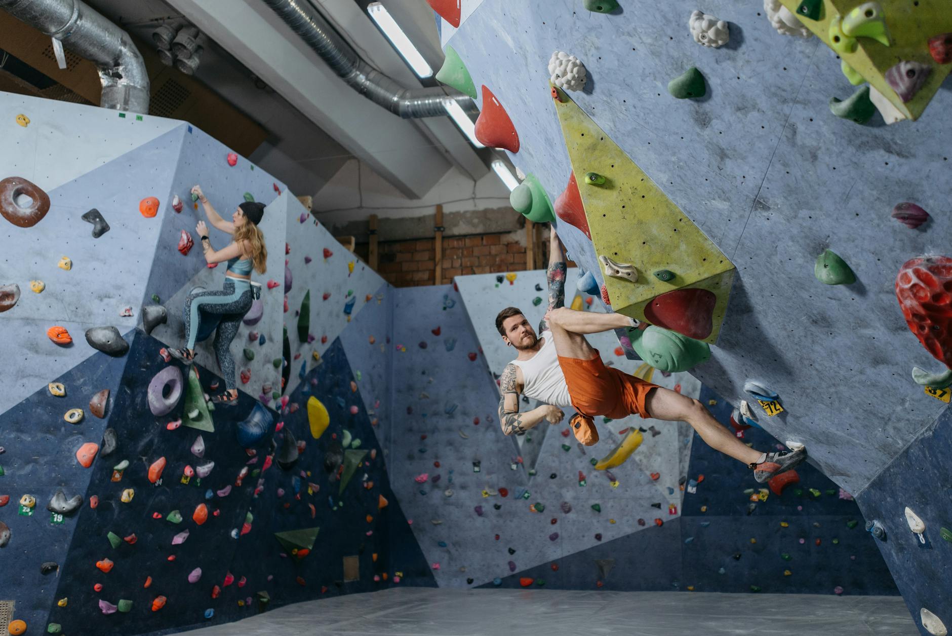 Dwóch wspinaczy na ściance boulderowej trenuje siłę chwytu i przedramion