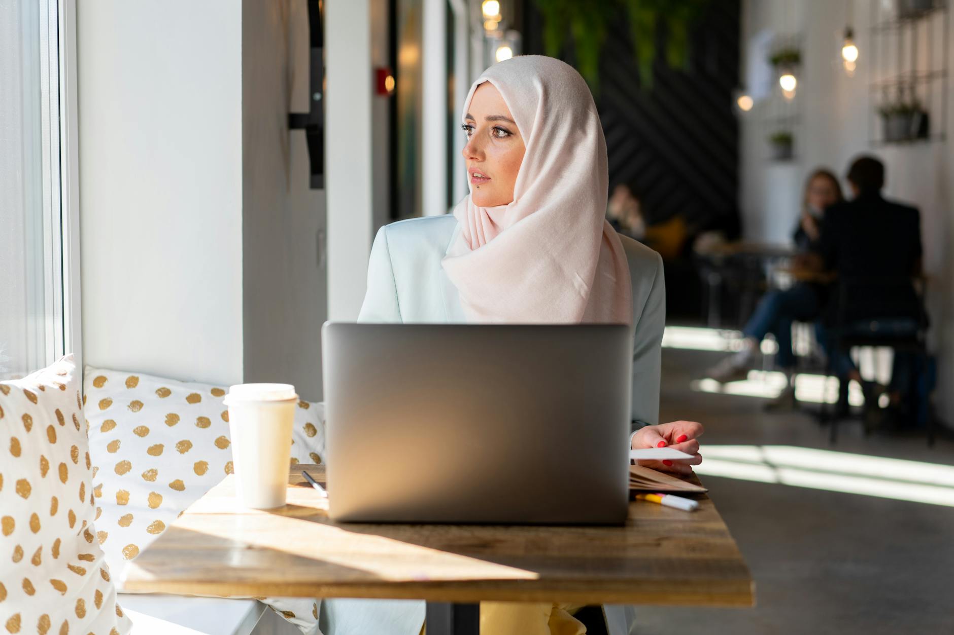 Muzułmanka w hijabie pracuje przy laptopie w kawiarni, zamyślona