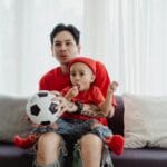 Ojciec i syn z piłką nożną siedzą razem na kanapie