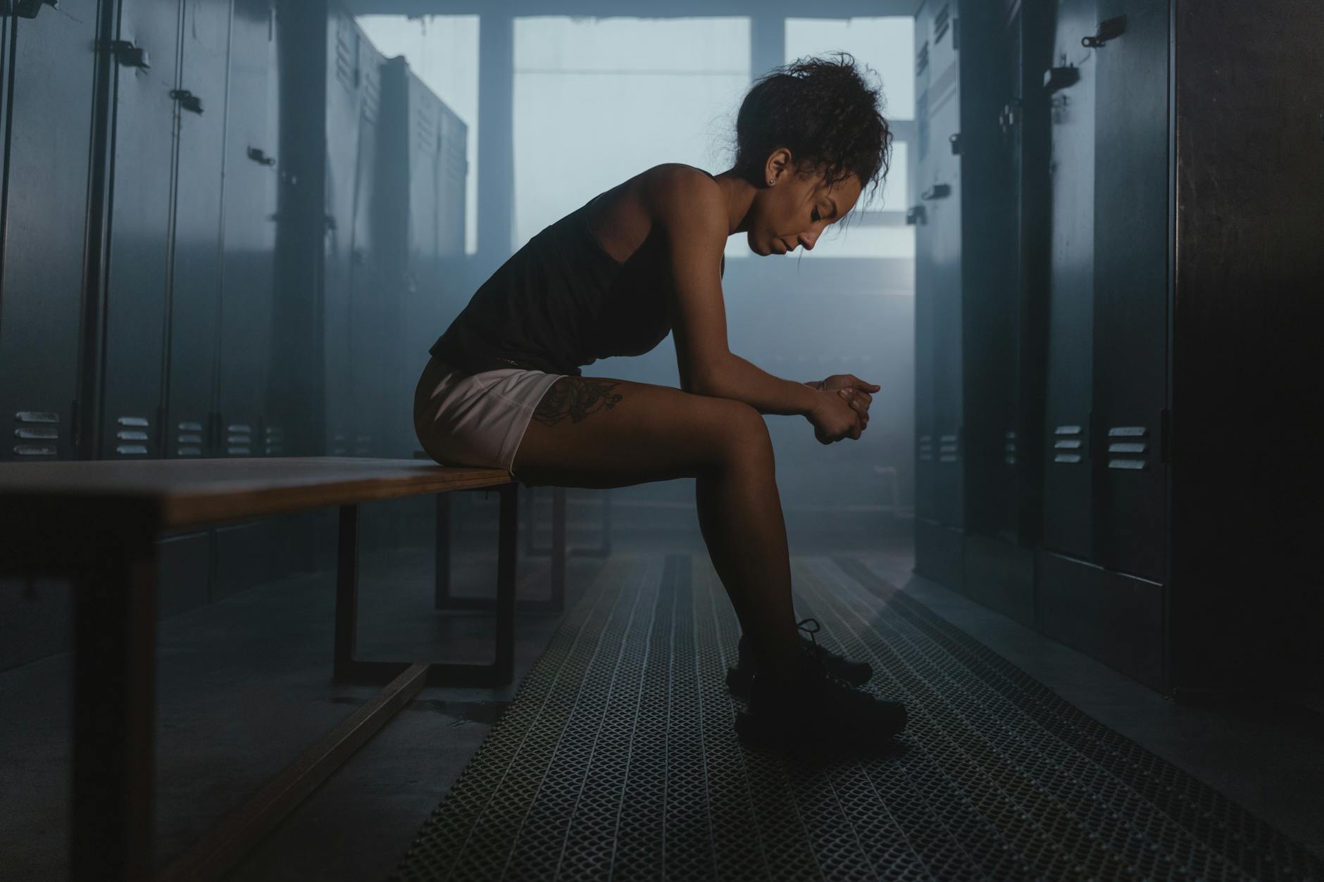 Zamyślony sportowiec siedzący samotnie w półmroczniej szatni