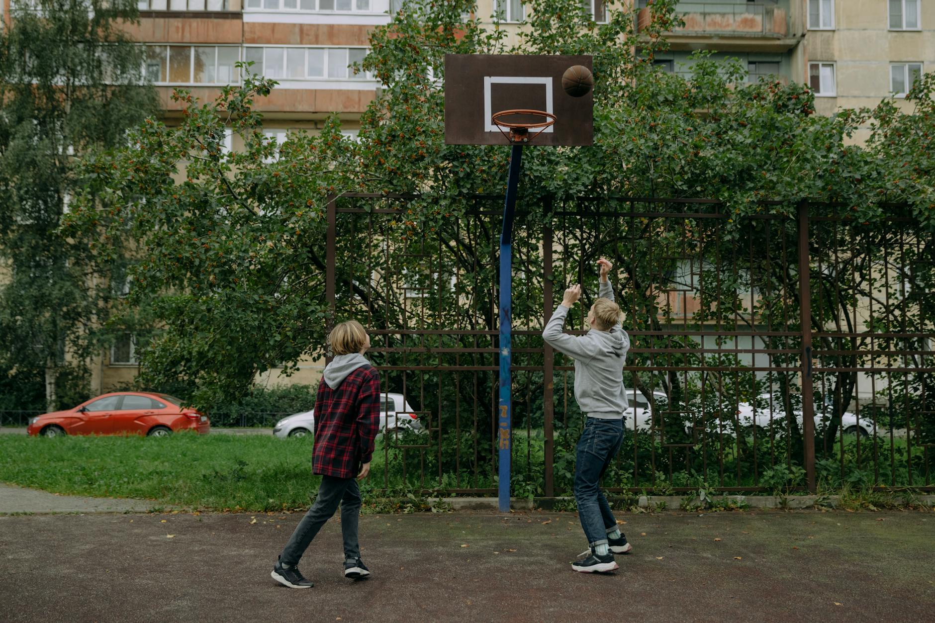 Dwójka rodzeństwa gra w koszykówkę na zewnętrznym boisku miejskim