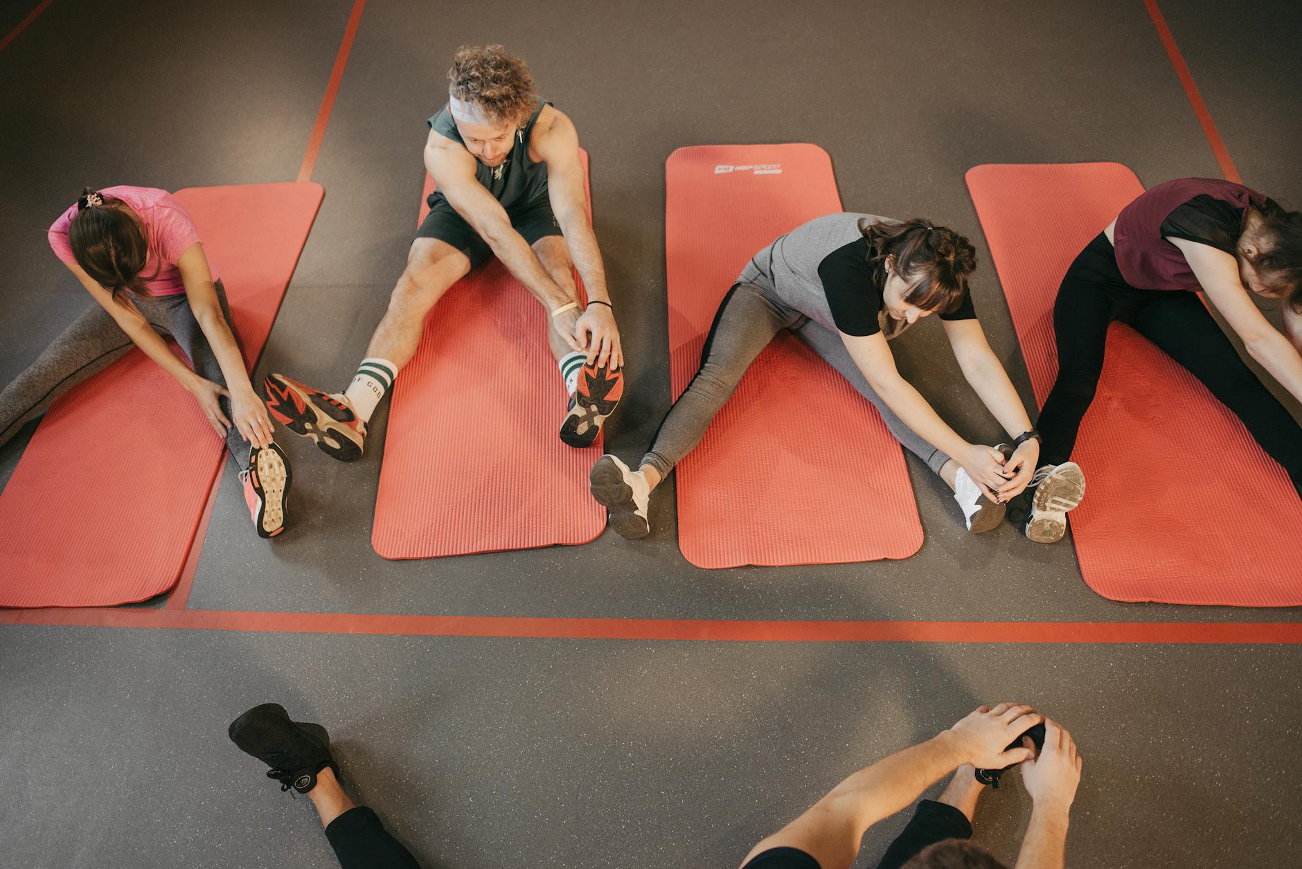 Grupa osób rozciąga się na czerwonych matach przed treningiem siłowym