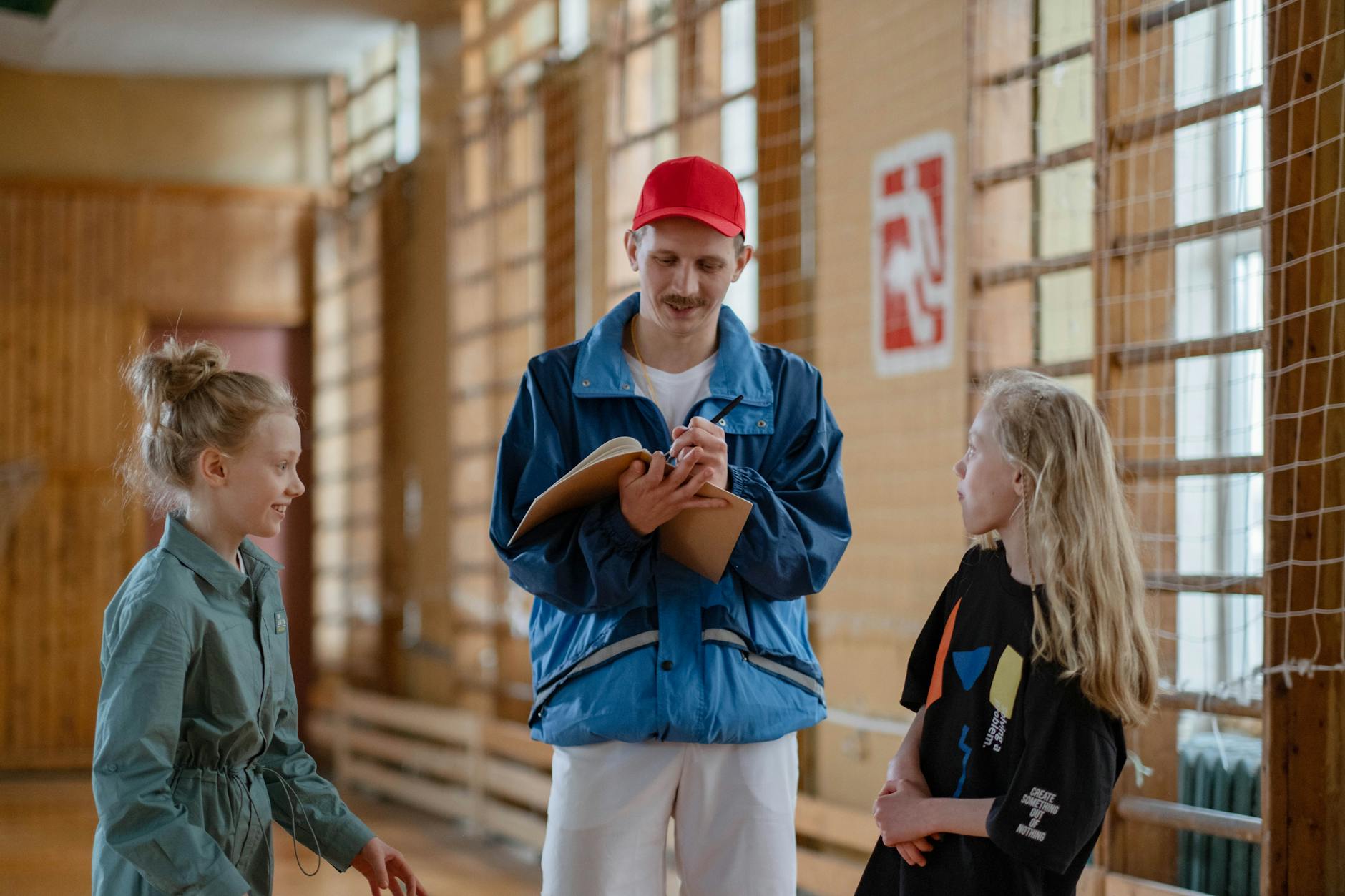 Trener rozmawia z dwiema dziewczynkami podczas zajęć sportowych w hali