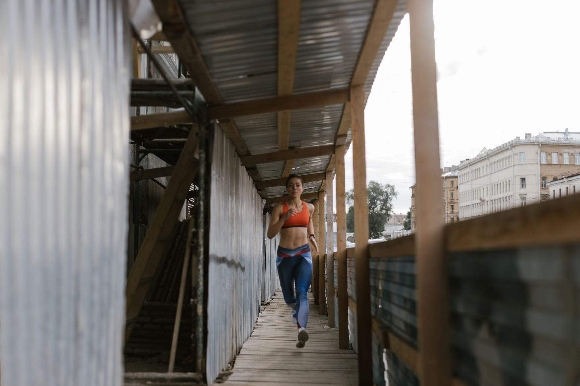 Kobieta w stroju sportowym biegnie w wąskim miejskim przejściu