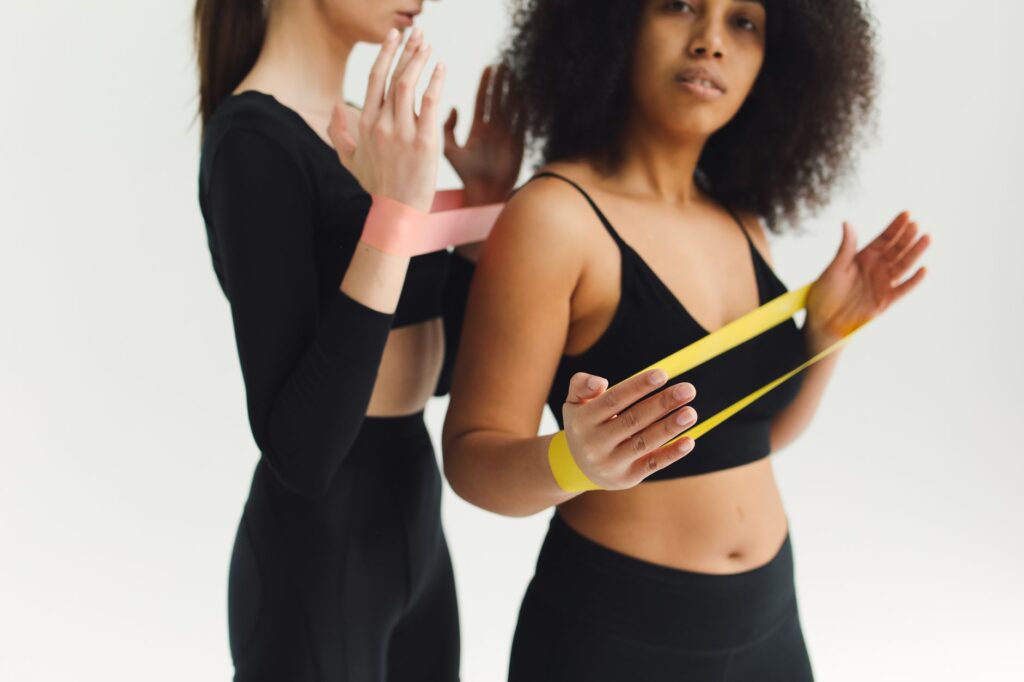 Dwie kobiety ćwiczą z gumami oporowymi w studio fitness